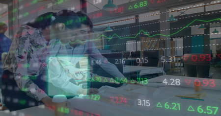 Leaning colleagues examining printed documents and typing on laptop in office, stock market overlay....
