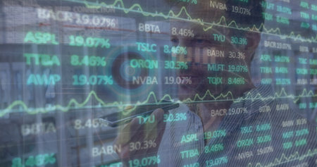Speaking into smartphone, man in shirt monitoring stocks on glass display at office, with tickers. Business, finance, technology, data, corporate, communication, professionalの写真素材