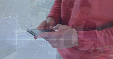 Holding smartphone, man in red sweater analyzing market charts at desk, with data overlays....