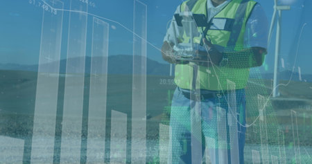 Operating technician wearing safety vest using joystick remote at wind turbine site, showing charts....