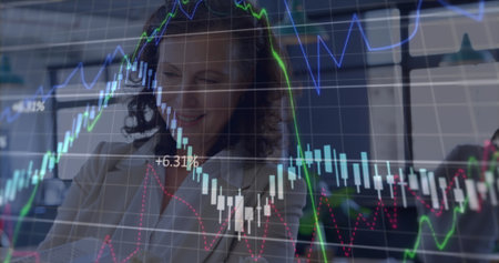 Reviewing suit-clad businesswoman studying financial charts in office, with document and monitors....