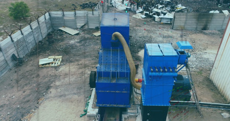Two large blue machines sitting on metal tracks in scrap yard, with corrugated hose and pallets....
