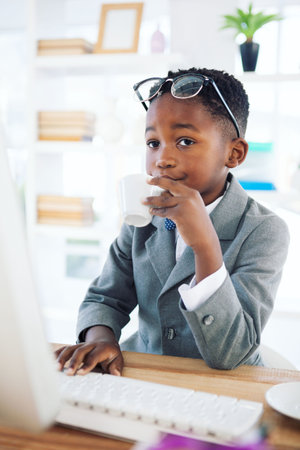 Businessman looking away while drinking coffee at deskの写真素材