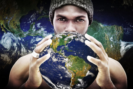 Man wearing beanie and silver ring is holding globe near face against flat backdrop with clouds. Cosmic, introspective, futuristic, contemplative, surreal, vibrant, planetaryの写真素材