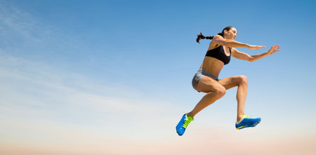 Female athlete long jumping against sky