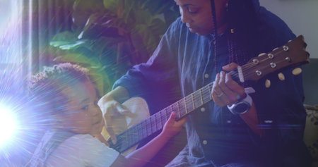 Mother in blue shirt guiding toddler strumming acoustic guitar near living room window, with plant. Family, mentorship, education, serene, harmony, nurturing, acousticの写真素材