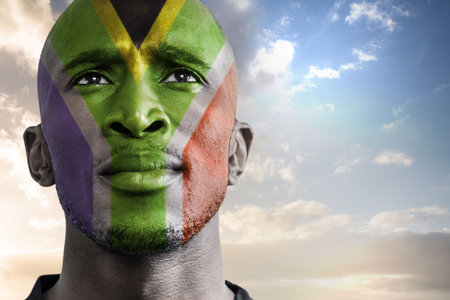 Portrait is showing man looking upward under sunrise sky, featuring South African flag face paint. Patriotism, celebration, nationalism, cultural, vibrant, outdoor, inspiringの写真素材