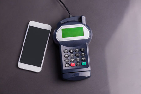 Flat design is showing smartphone and card terminal keypad resting on dark gray tabletop. Technology, commerce, contactless, digital, payment, modern, financeの写真素材