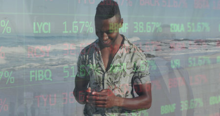 Holding smartphone, adult male wearing tropical shirt on sandy beach, with stock ticker overlay....