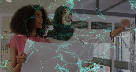 Unrolling blueprint two architects wearing hijab in studio, with digital projection. Collaboration, innovation, technology, architecture, workspace, professionalism, teamworkの写真素材