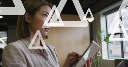 Holding tablet woman wearing grey blouse standing in modern office, with wood partition, plant....