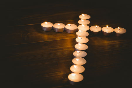Lit candles in shape of cross on wooden table