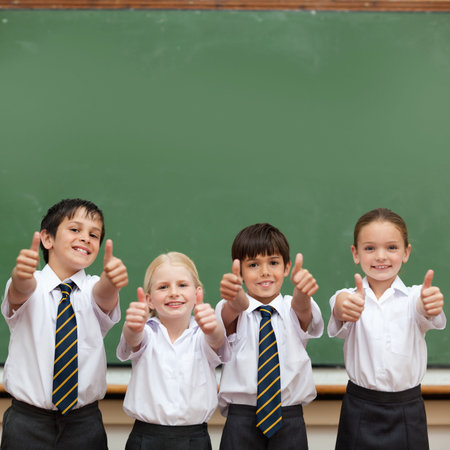 Cute pupils showing thumbs up in classroomの写真素材