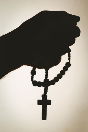 Close-up of silhouette hand holding rosary beadsの写真素材