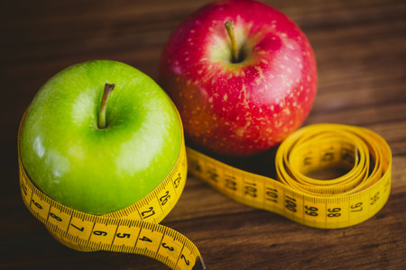 Red and green apples with measuring tape on wooden table