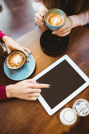 Cropped hands of caucasian woman with coffee on table pointing at tablet while talking with friend. Copy space, unaltered, friendship, together, drink, cafes, communication and technology concept.の写真素材