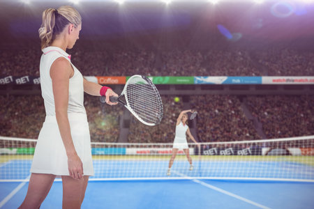 Young women playing tennis on court against fans in stadiumの写真素材