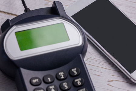 Flat design showing black payment terminal green screen keypad beside silver smartphone on tabletop....