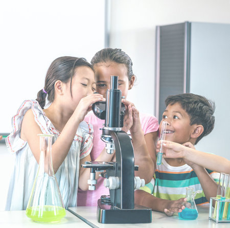 Happy school children in science lab using microscopeの写真素材