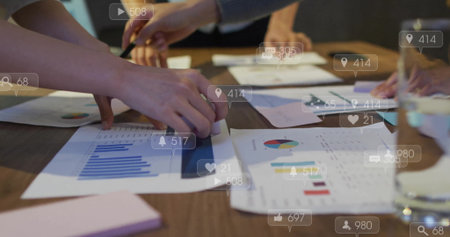 Examining professionals in suits pointing at printed graphs on meeting table with pen, sticky pad. Collaboration, teamwork, data analysis, business strategy, corporate meeting, professional environment, digital iconsの写真素材