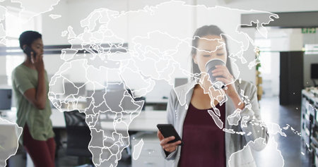 Two women sipping coffee holding smartphone and calling on phone in office with world map overlay. Collaboration, professionalism, technology, workspace, communication, productivity, modernの写真素材