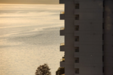 Flat illustration showing golden sunlight reflecting off rippled water with balconies and trees. Landscape, urban, minimalistic, tranquility, serenity, natural, modernの写真素材