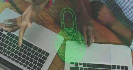 Discussing risks, two IT colleagues gesturing over laptops on wood desk, with green padlock overlay....