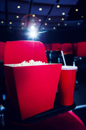 Drink with popcorn box on seat in illuminated theaterの写真素材