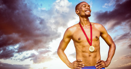 Shirtless athlete standing with hands on hip and medal against sky during sunset