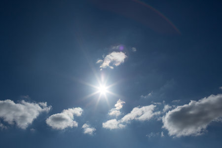 Sun is radiating rays in flat design with cumulus clouds and lens flare, copy space. Azure,...
