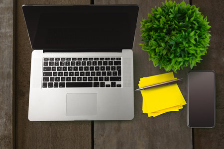 Silver laptop is sitting in flat design on wooden desk with smartphone, stationery items, plant. Workspace, productivity, modern, minimalism, office, technology, organizationの写真素材