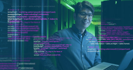 Standing Korean man holding laptop inside server room, with server racks and overlaid code text. Technology, data center, cybersecurity, digital, innovation, industrial, professionalの写真素材