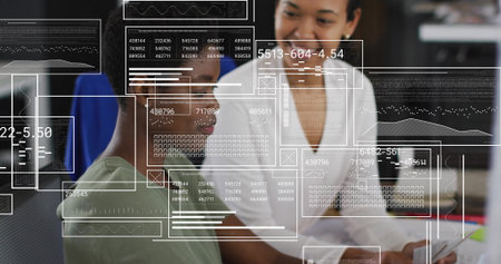 Collaborating colleagues in green and white tops analyzing computer data in office with data panels. Technology, teamwork, innovation, analytics, digital, professional, mentorshipの写真素材