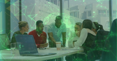 Team members leaning over laptop, documents, coffee cups around office table, with hologram globe. Collaboration, teamwork, digital, technology, innovation, business, modernの写真素材