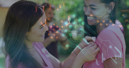 Pinning volunteer woman attaching pink ribbon onto matching pink T-shirt in park, circuit overlay. Support, advocacy, empowerment, unity, compassionate, outdoor, activismの写真素材