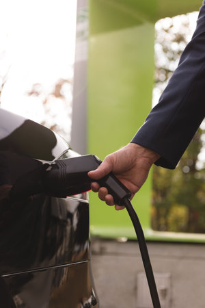 Close-up of man charging electric car at charging stationの写真素材