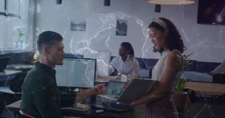 Discussing colleagues holding laptop and typing at open-plan office, with digital world map overlay....