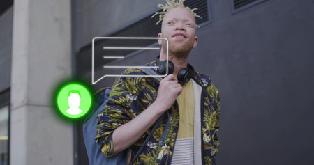 Looking upward man wearing printed jacket, backpack and headphones at facade with chat overlay....