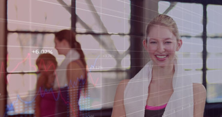 Standing female in sleeveless top draping towel around neck in gym with digital charts, copy space....
