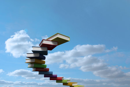 Books are floating in spiral staircase formation in flat vector style against blue sky with clouds. Surrealism, imagination, inspiration, vibrant, whimsical, creativity, fantasyの写真素材