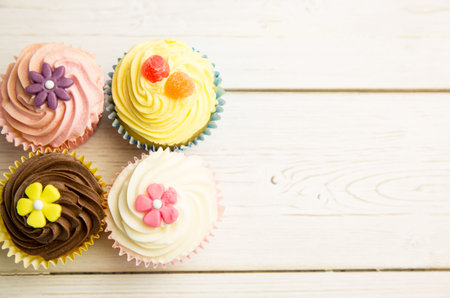 Showing four cupcakes on tabletop, showcasing pastel frosting, fondant flowers, gummies. Desserts, confections, baked goods, artisanal, pastel, celebration, rusticの写真素材