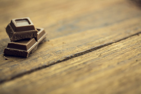 Chocolate squares are resting on rustic wooden plank surface with grain knots in 3D render. Dessert, gourmet, handcrafted, artisanal, textured, warm tones, minimalismの写真素材