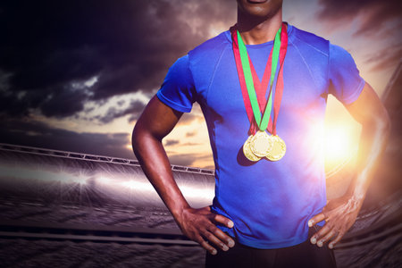 Midsection of male athlete standing with hands on hip at stadium during sunsetの写真素材