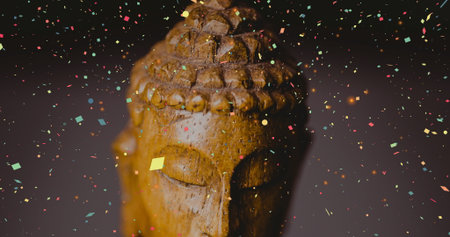 Carved wooden Buddha head statue sitting in studio, with multicolored confetti floating around. Meditation, spirituality, zen, tranquility, celebration, abstract, craftの写真素材