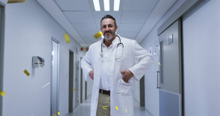 Standing middle-aged male doctor in hospital corridor, with stethoscope and floating confetti. Professional, healthcare, celebration, medical, clinical, wellness, hospitalの写真素材