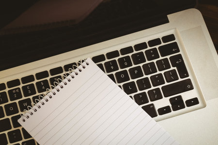 flat design art is showing blank spiral notebook diagonally across laptop keyboard on wooden desk....