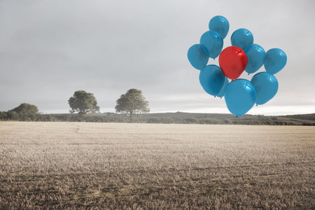 Helium balloon cluster is floating over stubble field with distant trees in flat design, cloudy sky. Landscape, tranquility, minimalism, celebration, outdoor, elevation, serenityの写真素材