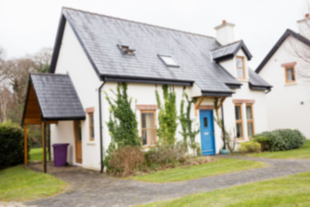 White cottage-style house is standing by curved driveway, showing blue door, slate roof and porch. Charm, rural, suburban, architecture, landscape, vintage, cozyの写真素材