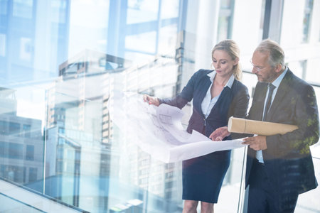 Digital composite image of business people discussing over blueprint in office