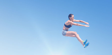 Full length of female athlete long jumping against blue skyの写真素材